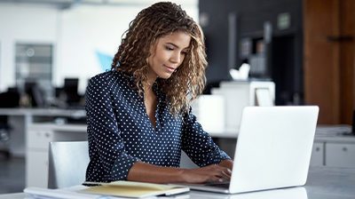 A woman typing on her laptop while sitting at a desk in an office 